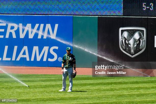 Left fielder Mark Canha of the Oakland Athletics waits for the sprinklers to be turned off during the sixth inning against the Cleveland Indians at...