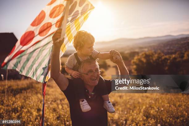 grandfather and grandson running a kite outdoors - kite flying stock pictures, royalty-free photos & images