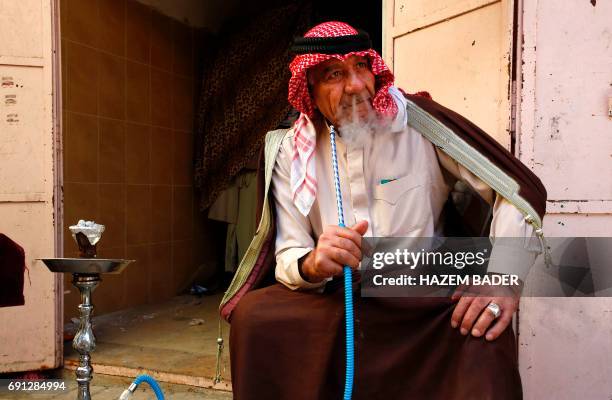 Eid Jaabari, a Palestinian man wearing a traditional keffeyah on his head, smokes a waterpipe in the old city of Hebron on May 8, 2017 in the Israeli...