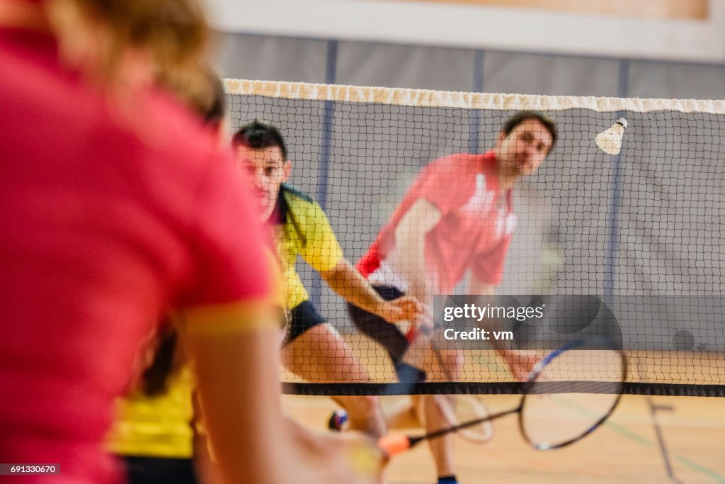 Two women playing badminton against two men