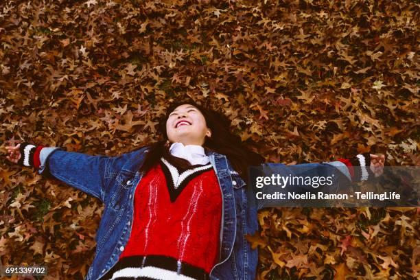 a young chinese woman laying down and playing with autumn leaves - green and red autumn leaves australia stock pictures, royalty-free photos & images