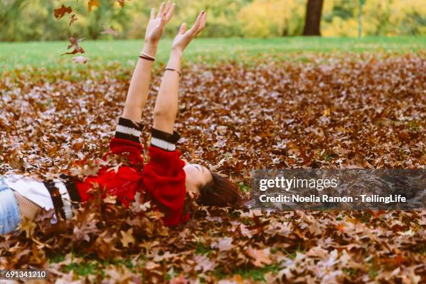 a young chinese woman laying down and playing with autumn leaves - green and red autumn leaves australia stock pictures, royalty-free photos & images