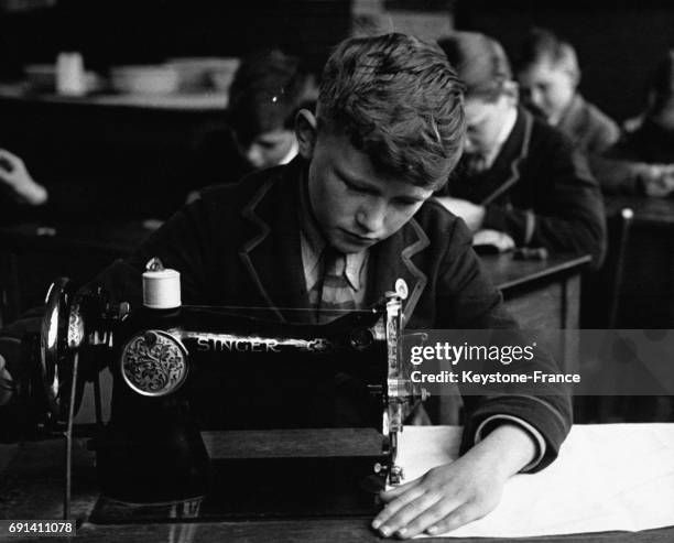 Un adolescent de 11 ans utilisant une machine à coudre dans une école de couture, circa 1950, à Londres, Royaume-Uni.