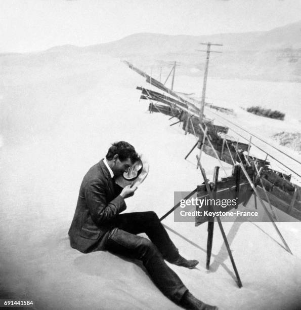 Homme assis sur une dune de sable se protège le visage avec son chapeau, au bord de la rivière Columbia, Oregon, Etats-Unis au début du XXe siècle.