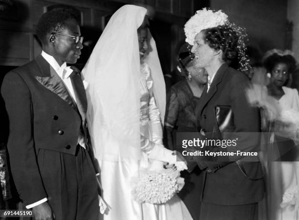 Madame Georges Bidault félicite les jeunes époux, le député sénégalais Léopold Sédar Senghor et Ginette Eboué, fille du premier gouverneur général...