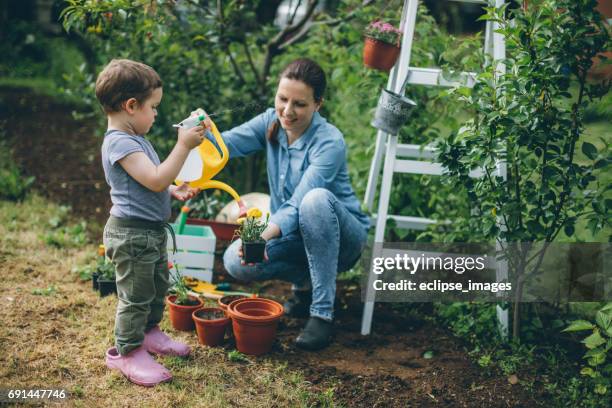 toddler boy and his mother watering plants in the garden - small village countryside stock pictures, royalty-free photos & images