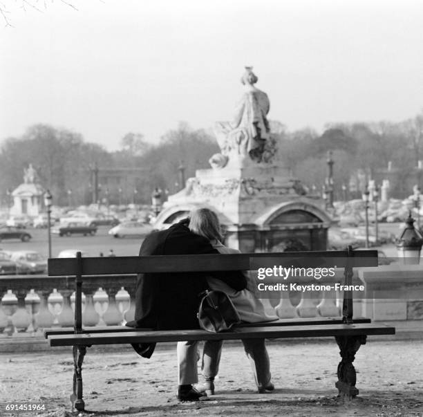 Couple d'amoureux assis sur un banc au soleil au Jardin des Tuileries à Paris, France le 16 janvier 1968.