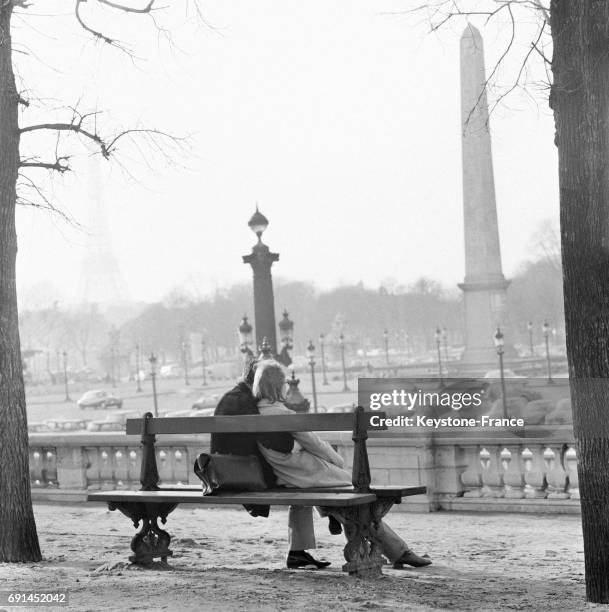 Couple d'amoureux assis sur un banc au soleil au Jardin des Tuileries à Paris, France le 16 janvier 1968.