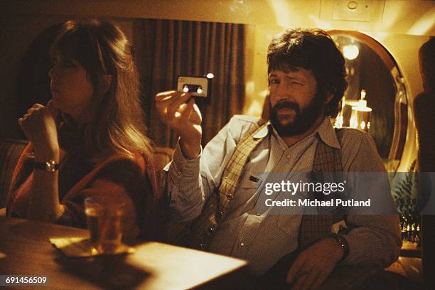 English guitarist Eric Clapton holding an audio cassette tape on board a private jet, USA, 1978. With him is his girlfriemd, model Pattie Boyd.