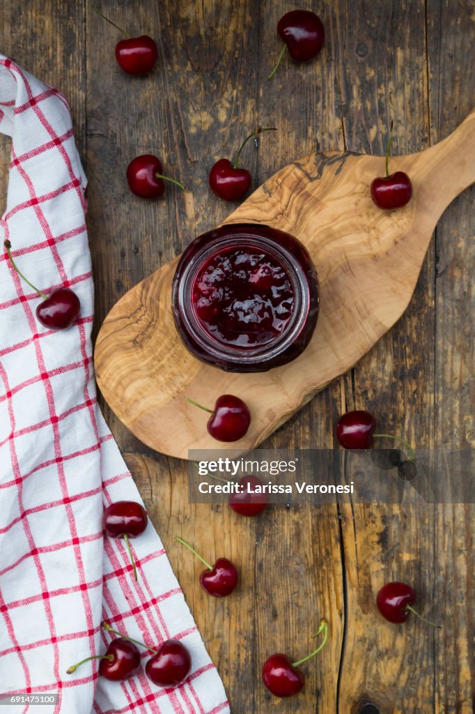 Jar of homemade cherry jam and cherries on wood