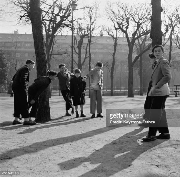 Un groupe de jeunes hommes jouent à la pétanque dans le Jardin du Palais Royal sous le soleil, à Paris, France le 2 mars 1953.