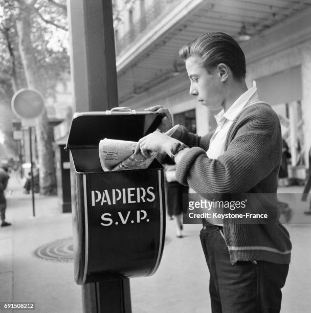 Un jeune homme jette son journal dans une poubelle installée dans une rue de Paris, France en 1954.