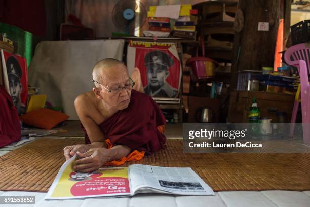 An older Monk reads a newspaper in front of a poster of General Aung San, father of Aung San Suu Kyi, at the Masoeyein Monastery on June 1, 2017 in...