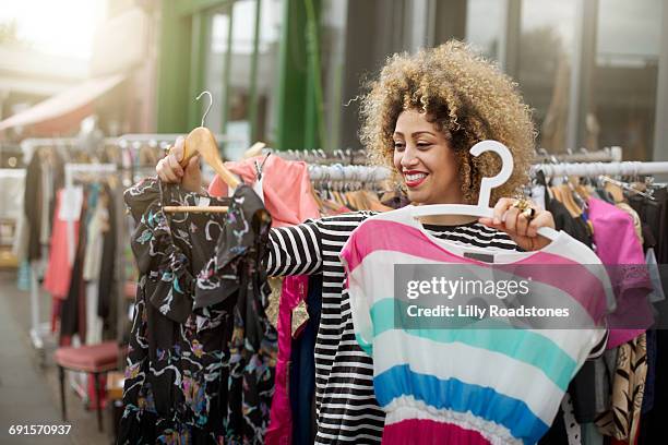 woman deciding between two dresses at market - multi colored dress photos et images de collection