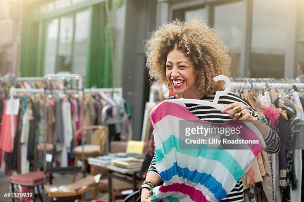 woman laughing while trying on clothes at market - clothes fotografías e imágenes de stock