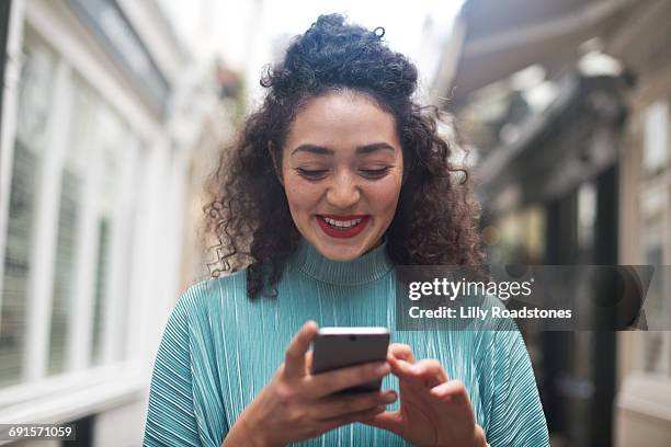 young woman texting in lane of shops - good news stock pictures, royalty-free photos & images