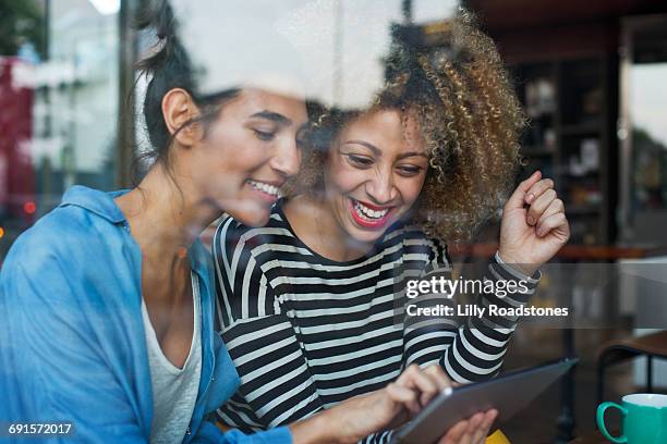 two woman using tablet computer in coffee shop - sharing two people stock pictures, royalty-free photos & images