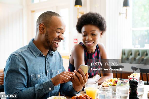 two people looking at phone with lunch. - woman sitting on mans lap stockfoto's en -beelden