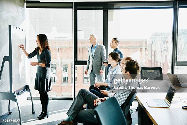 businesswoman leading presentation at whiteboard - 50s woman writing at table imagens e fotografias de stock