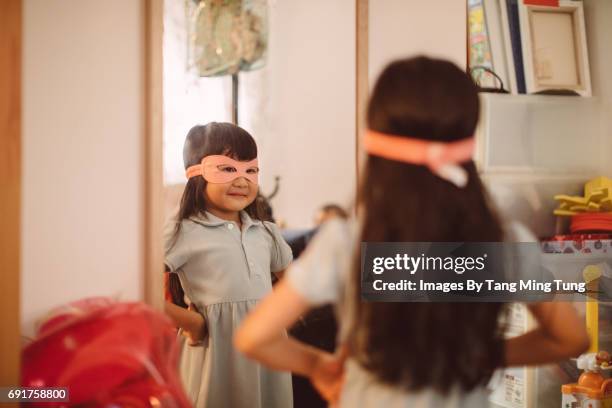 lovely little girl wearing a superwomen mask looking into the mirror with pride - arms akimbo stock pictures, royalty-free photos & images