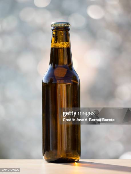 bottle of beer of crystal with metallic cap on a table outdoors illuminated by the light of the sun - garrafa de cerveja imagens e fotografias de stock