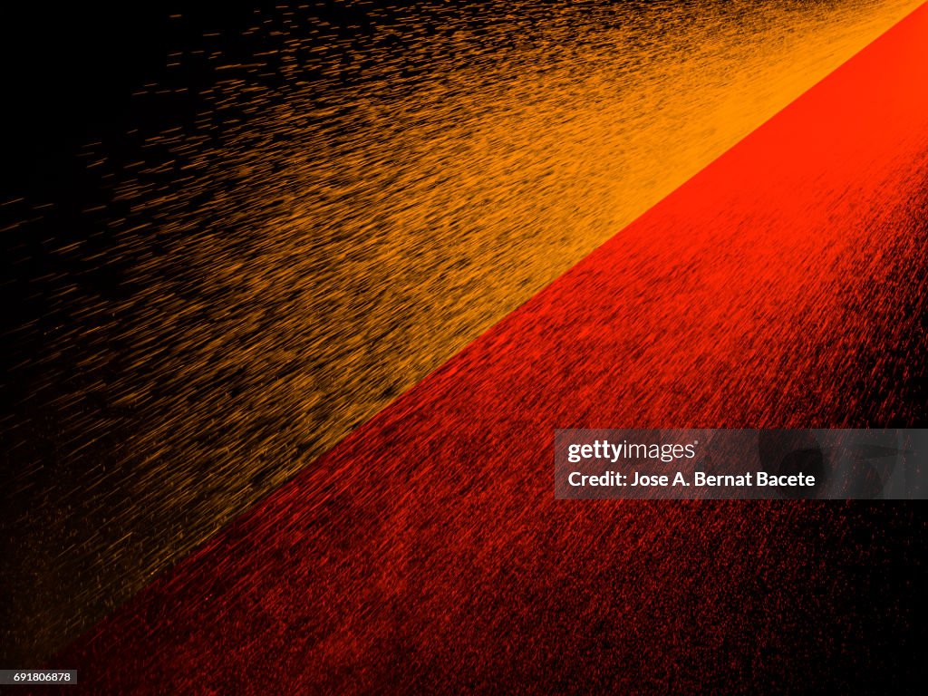 Explosion of water drops of colors red and orange, floating in the air on a black background