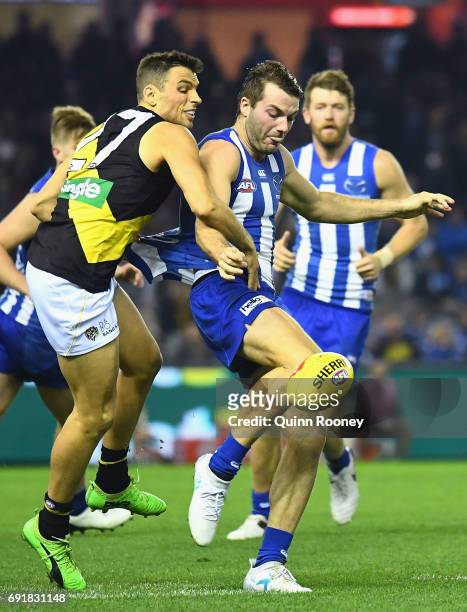 Luke McDonald of the Kangaroos kicks whilst being tackled by Sam Lloyd of the Tigers during the round 11 AFL match between the North Melbourne...