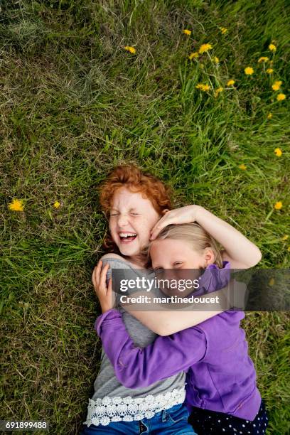 zwei verspielte kleine mädchen im frühling auf dem rasen liegen. - cousins stock-fotos und bilder