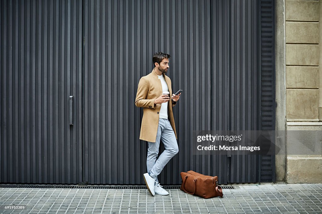 Businessman with phone and cup looking away