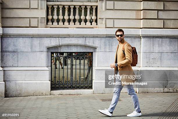 businessman walking on sidewalk by building - bürgersteig stock-fotos und bilder