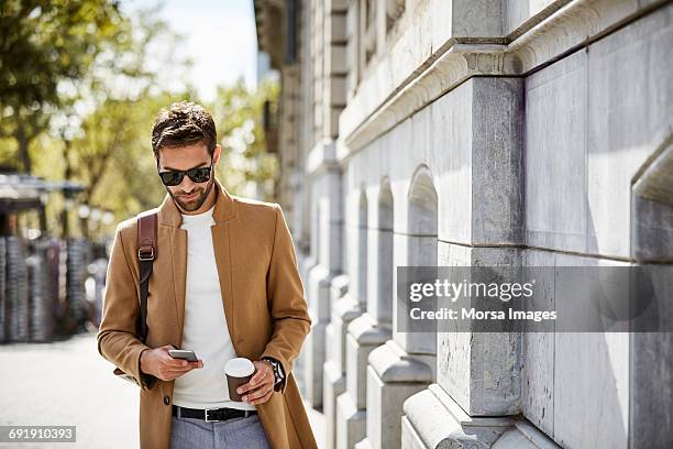 businessman using phone while holding cup in city - uomini di età media foto e immagini stock