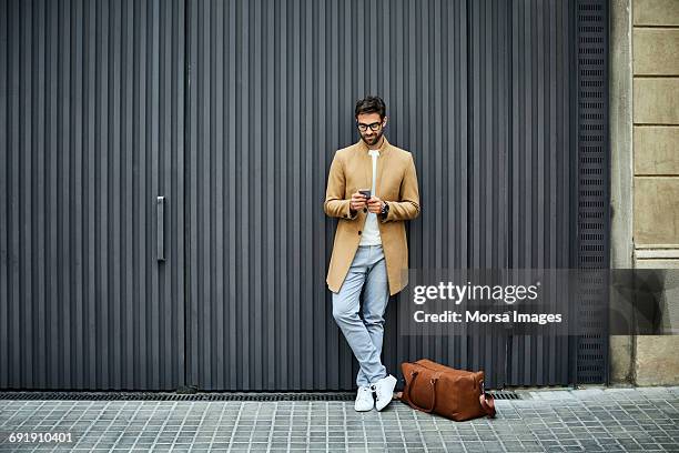 businessman texting on mobile phone against wall - gente mirando moviles fotografías e imágenes de stock