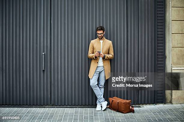 businessman texting on mobile phone against wall - de pé imagens e fotografias de stock