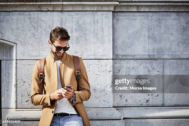 smiling businessman using phone against building - men phone stock-fotos und bilder