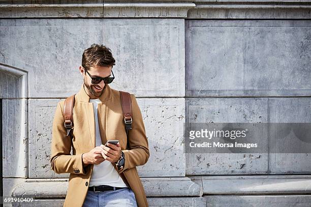 smiling businessman using phone against building - man celular ストックフォトと画像