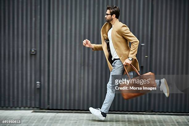businessman with bag running on sidewalk in city - carrera fotografías e imágenes de stock
