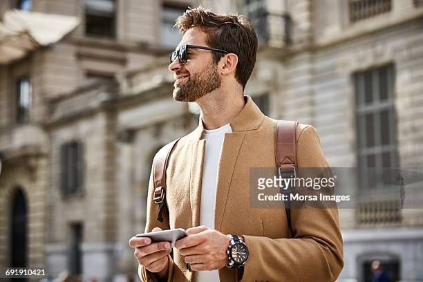 smiling businessman holding phone and looking away - orologio da polso foto e immagini stock