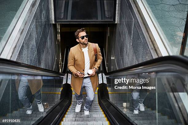 executive holding smart phone and cup at escalator - escalator photos et images de collection