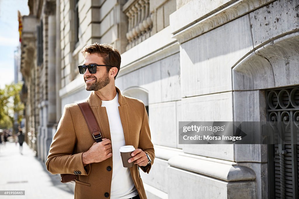 Smiling businessman with cup looking away in city