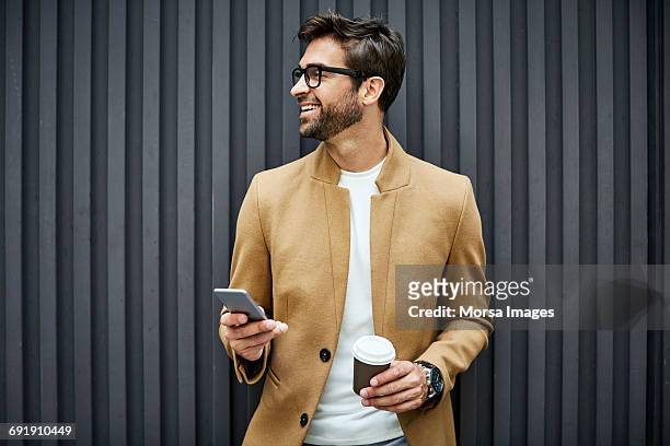 smiling businessman with smart phone and cup - eleganz stock-fotos und bilder