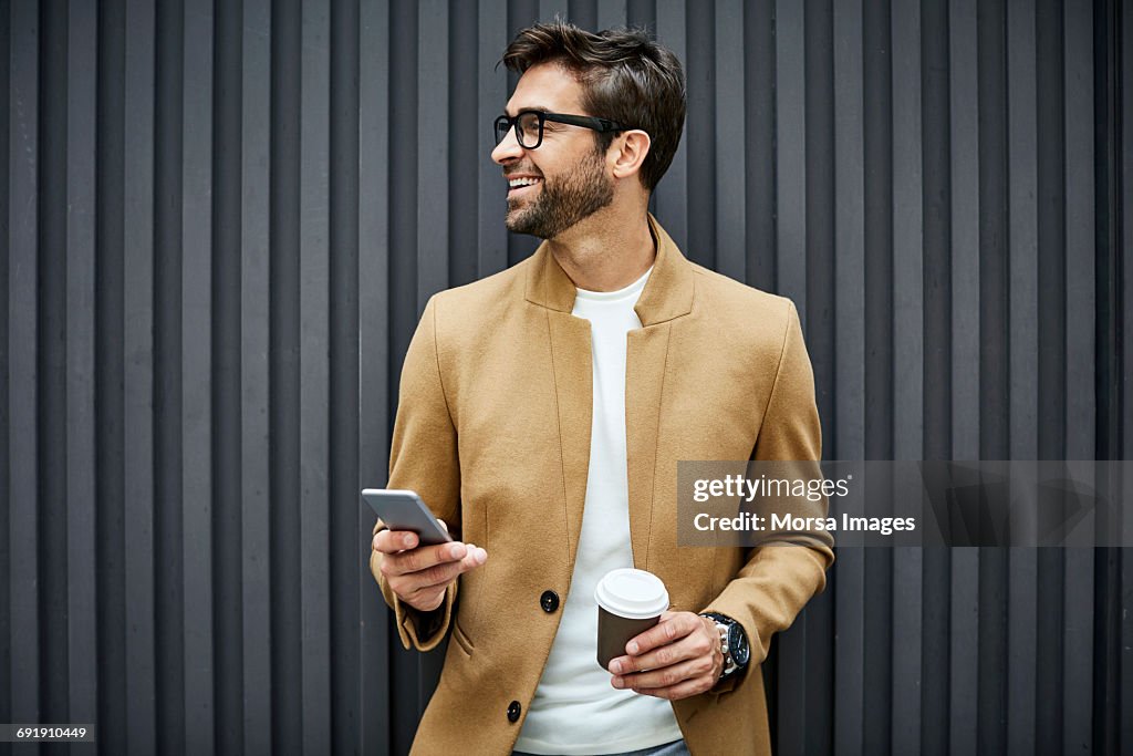 Smiling businessman with smart phone and cup