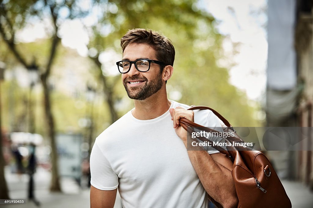 Smiling businessman with brown bag walking in city