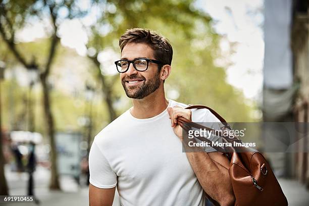 smiling businessman with brown bag walking in city - schöne menschen stock-fotos und bilder