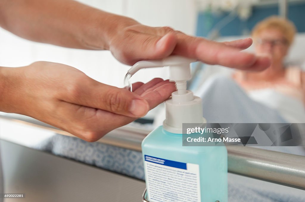 Nurse using hand sanitiser on hospital bed