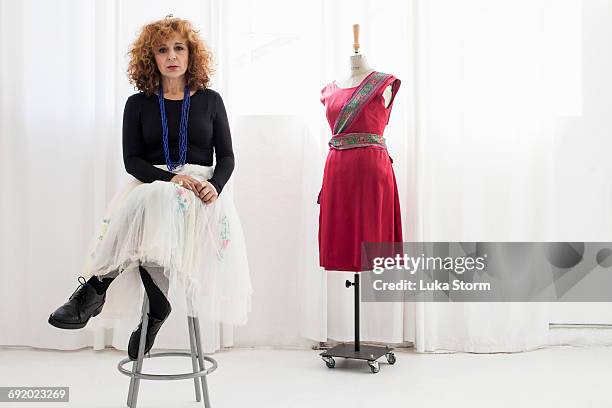 woman sitting on stool by tailors dummy looking at camera - manichino da sarto foto e immagini stock