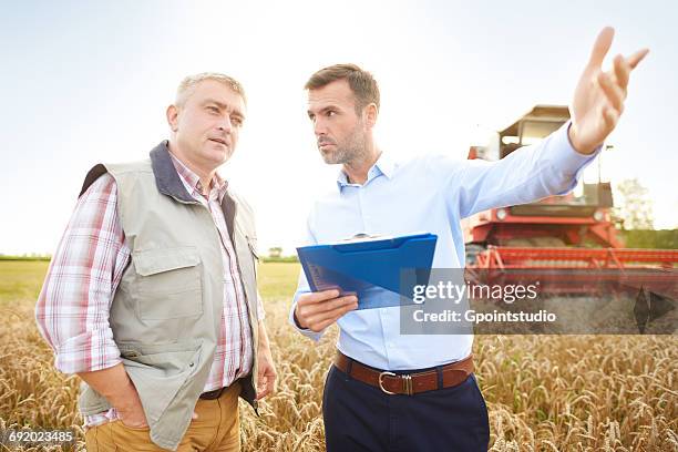 farmer and businessman in wheat field holding clipboard looking away - combine day 2 stockfoto's en -beelden