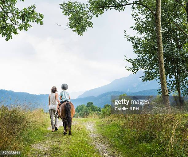 rear view of mother guiding son riding horse, fuessen, bavaria, germany - riding hat fotografías e imágenes de stock