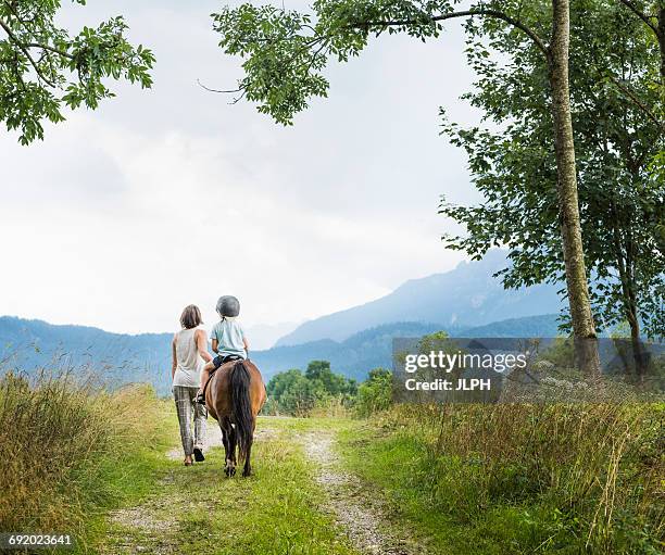 rear view of mother guiding son riding horse, fuessen, bavaria, germany - 乗馬帽 ストックフォトと画像