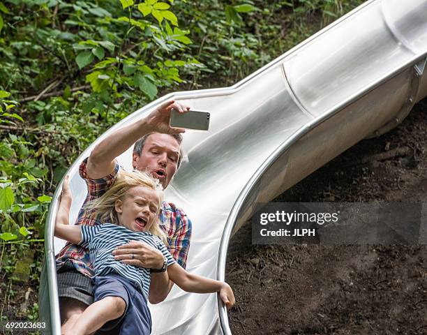 father and son sliding down slide holding smartphone - glijden stockfoto's en -beelden