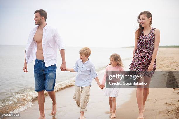 family holding hands walking on beach - mini shorts stock pictures, royalty-free photos & images